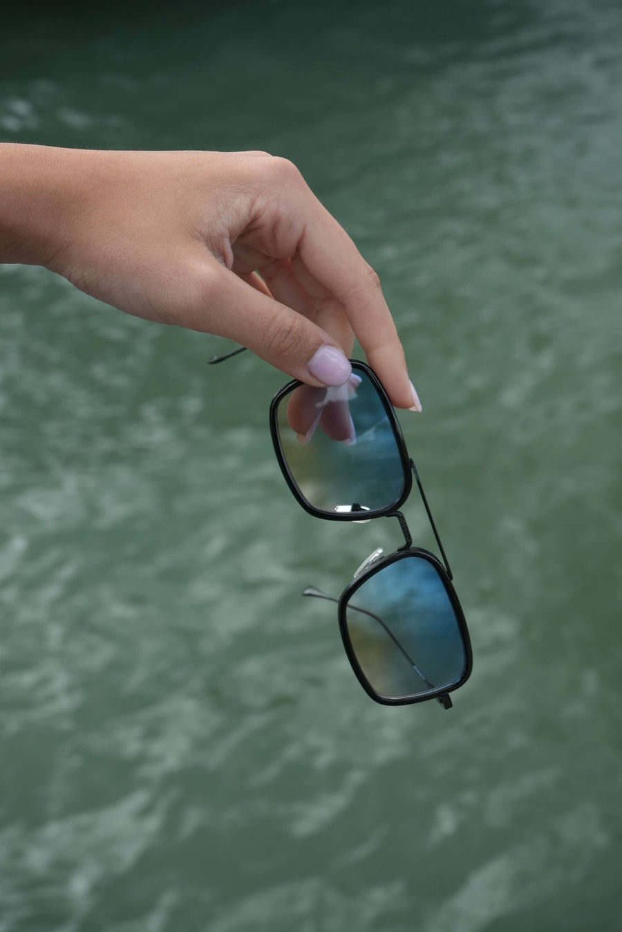 Hand holding SIMI sunglasses over the water